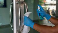 Person in protective gloves cleaning a door handle with a disinfection spray and disposable wipes